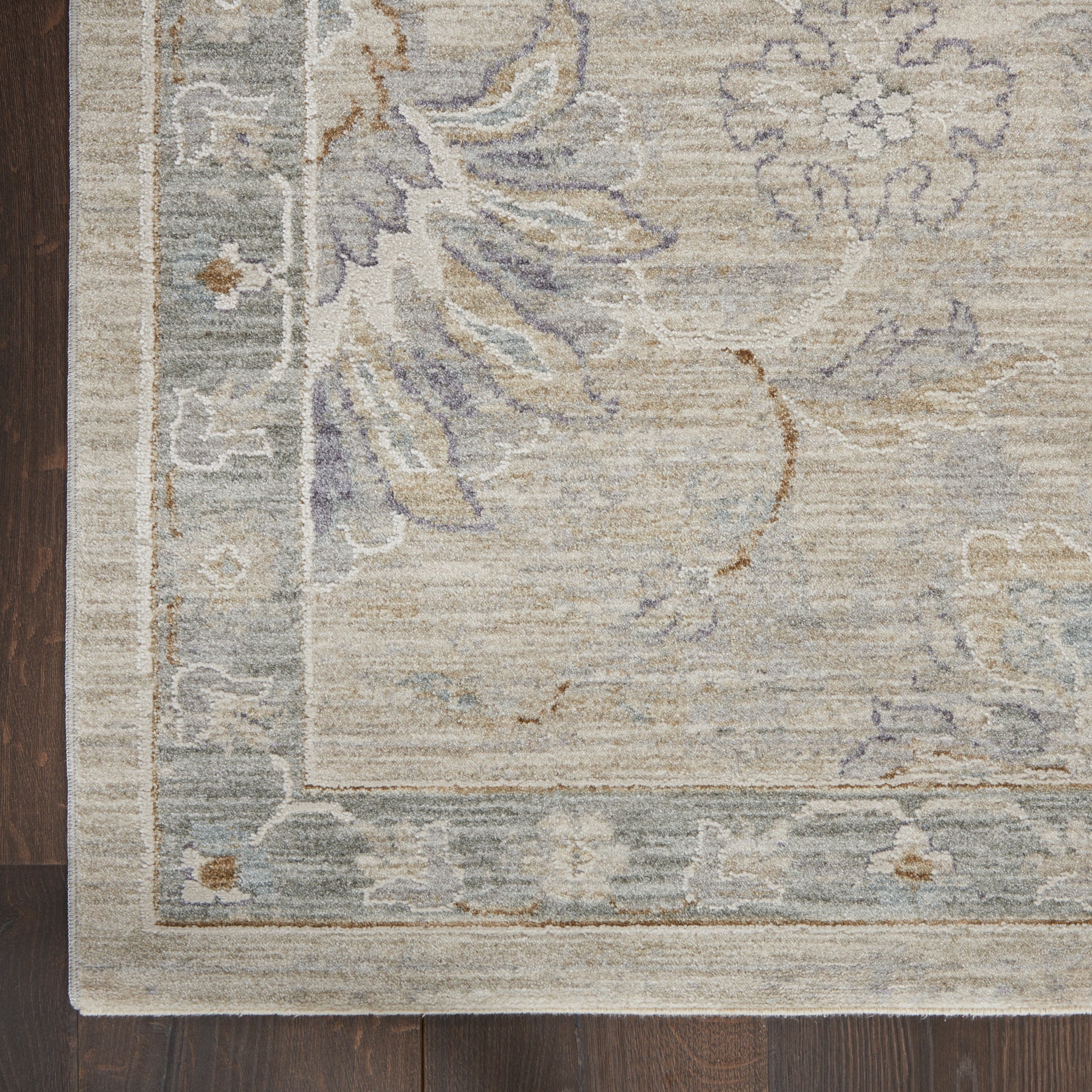 Vintage-inspired beige floral area rug with pale blue-gray flowers and a bordered edge on dark wood floor.