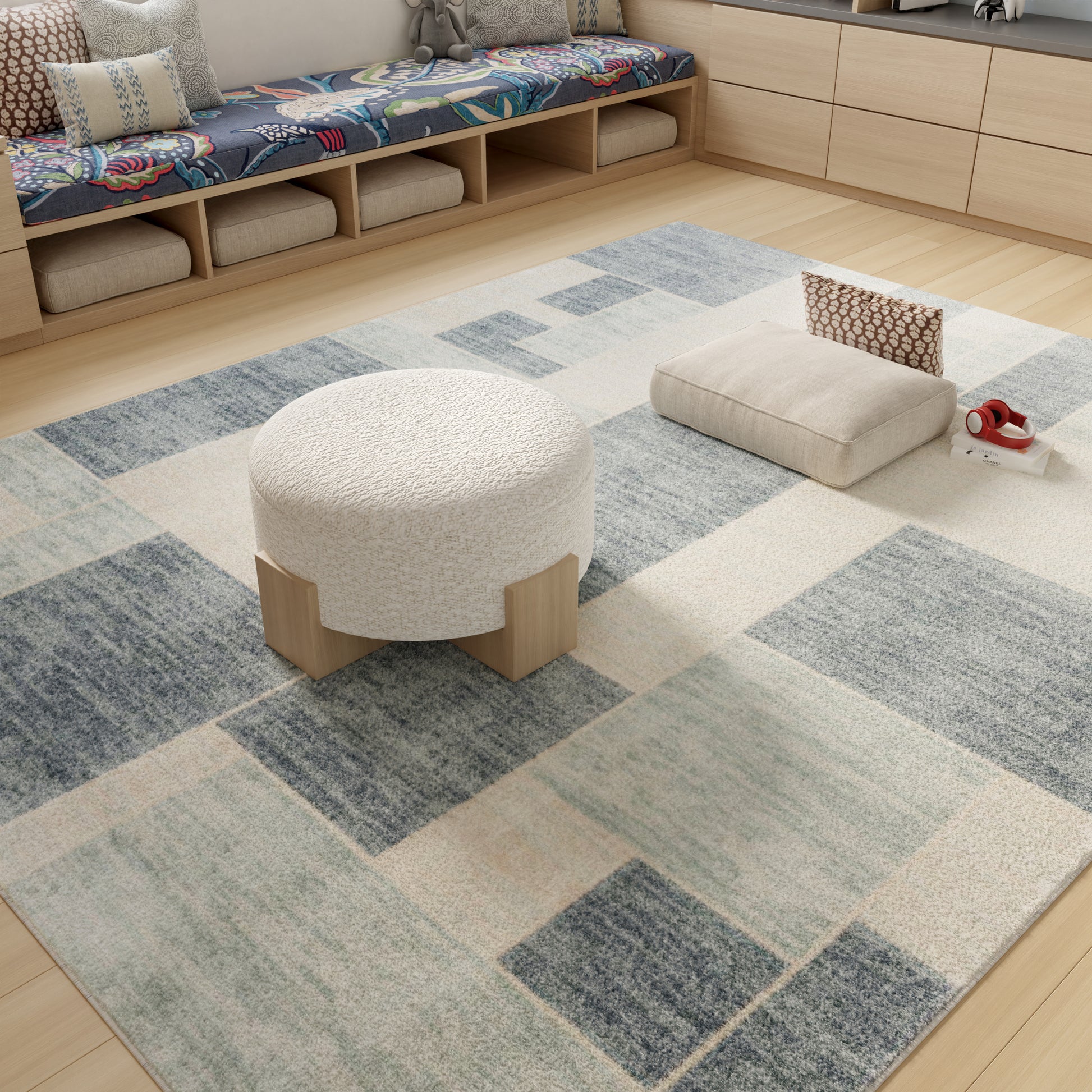 Cream boucle round ottoman with light wood legs on a blue-gray patchwork rug in a modern living room.