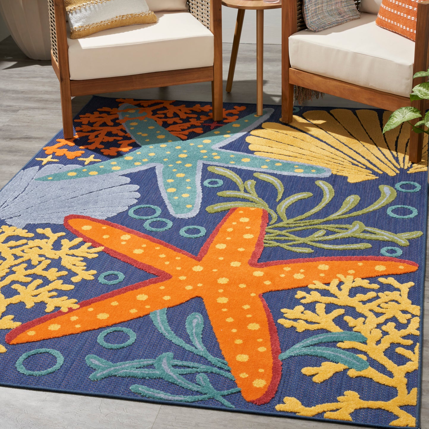 Outdoor rug with sea-life scene: bright orange starfish on blue sea, yellow coral, and green seaweed; near wooden chairs, 5' x 8'.