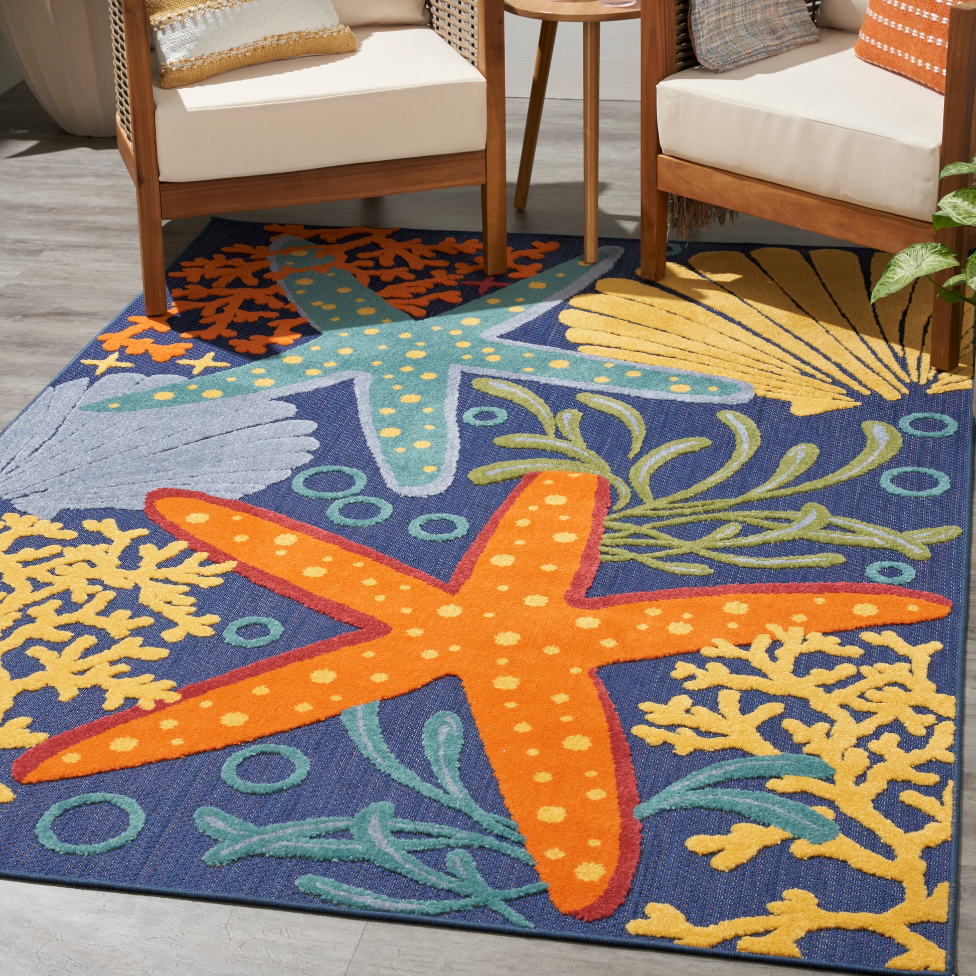 Outdoor rug with sea-life scene: bright orange starfish on blue sea, yellow coral, and green seaweed; near wooden chairs, 5' x 8'.