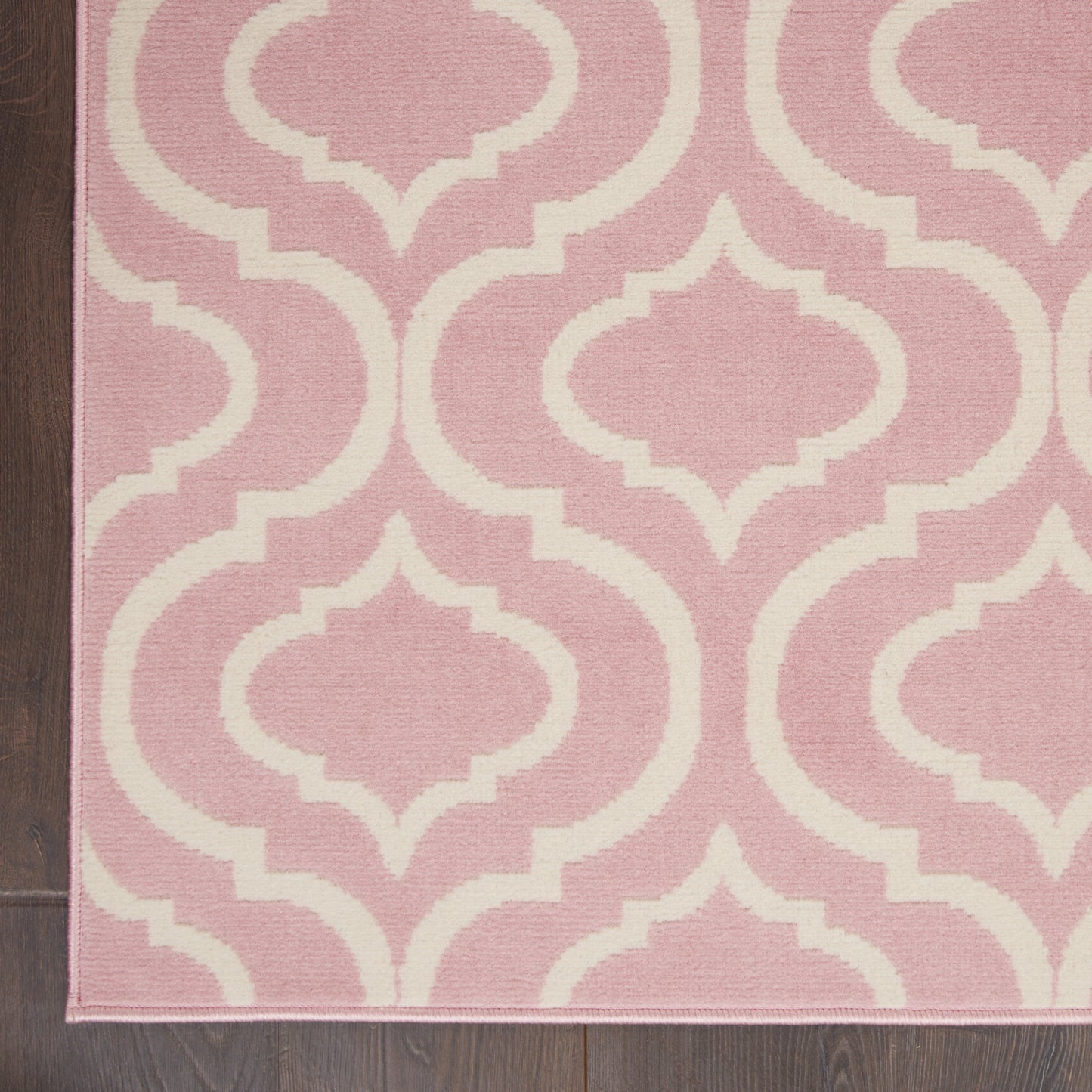 Pink rug with white Moroccan trellis pattern, soft geometric lattice; edge visible on dark wood floor.