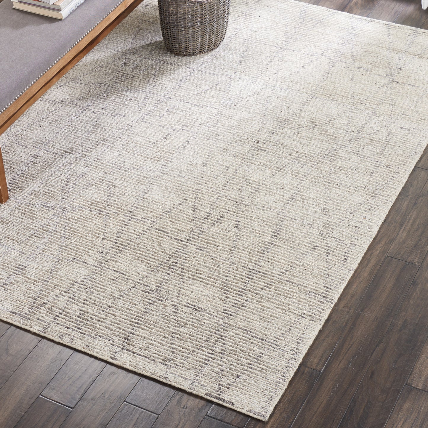 Beige rectangular rug with a subtle geometric square pattern on dark wood floor beside a wooden coffee table.