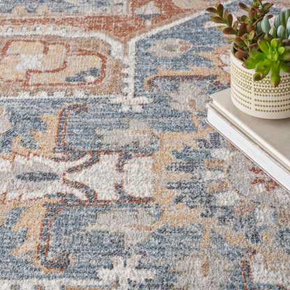 Close-up of an oriental rug in blue, tan and orange; white pot with gold dotted pattern and succulents atop stacked books.
