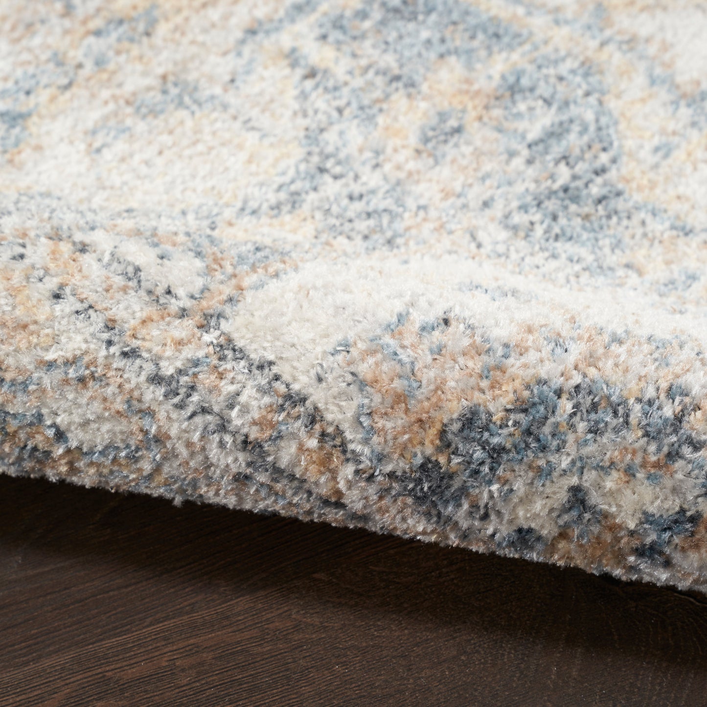 Soft, plush shag rug in blue, beige, cream and gray tones with a mottled abstract pattern on a dark wood floor.