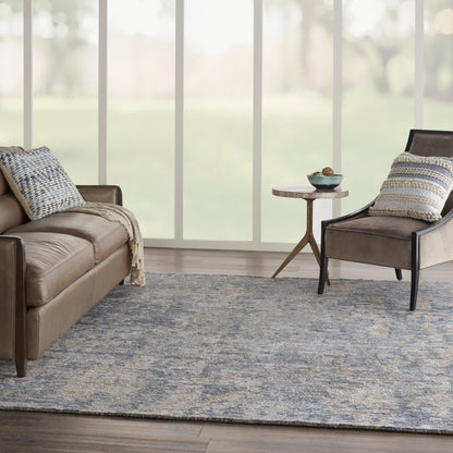 Brown leather sofa and matching chair, blue-gray area rug, neutral throws, small round side table under large windows.