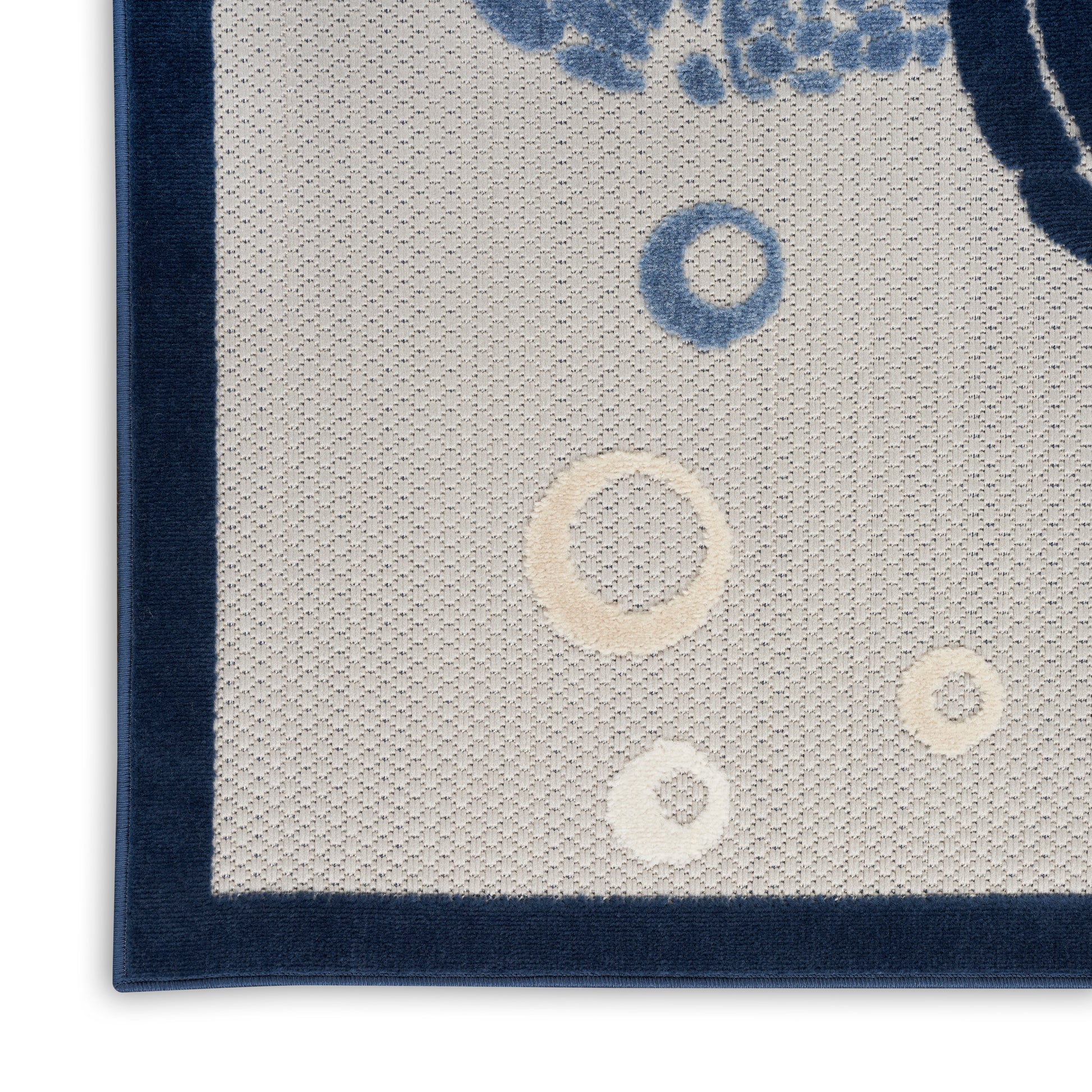 Beige textured woven rug with dark navy border and scattered blue and cream ring motifs.