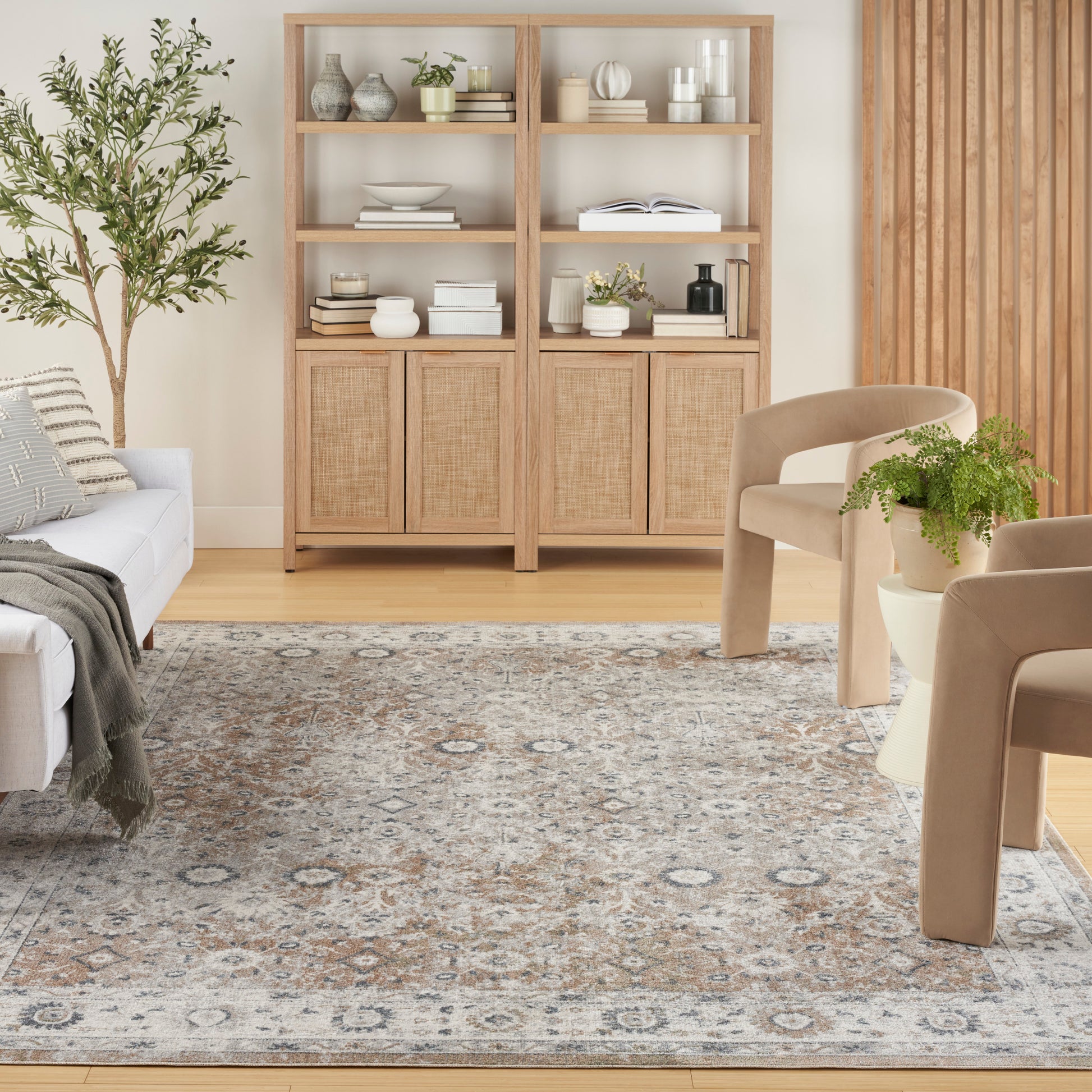 Light oak bookcase with woven cabinet doors, open shelves, beige chairs, plant, and a patterned rug in a calm living room.