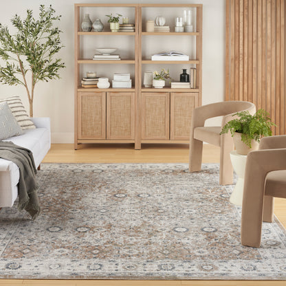 Light oak bookcase with woven cabinet doors, open shelves, beige chairs, plant, and a patterned rug in a calm living room.
