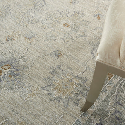 Soft beige-gray ornate patterned area rug with taupe accents beside a beige upholstered chair on a tapered metal leg.