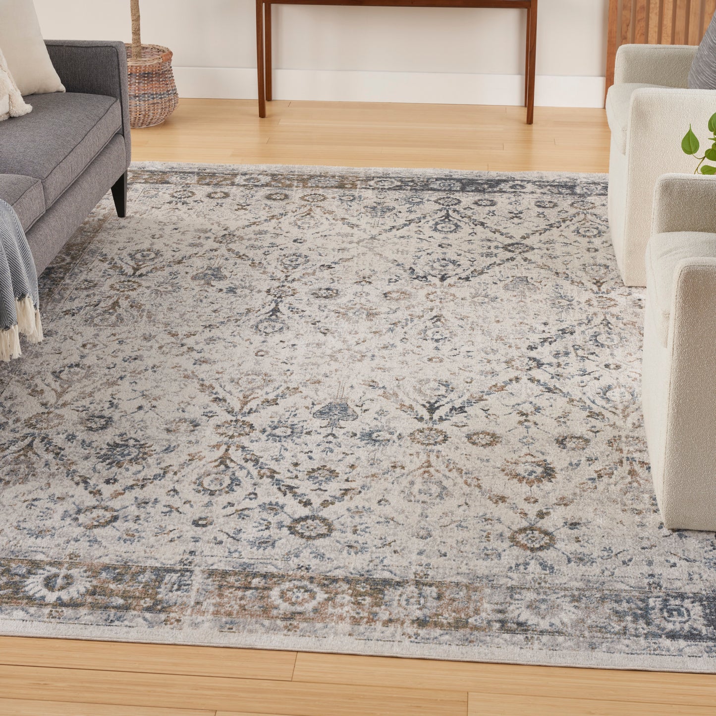 Grey and ivory patterned area rug in a contemporary living room with light wood floors, grey sofa and beige chairs.