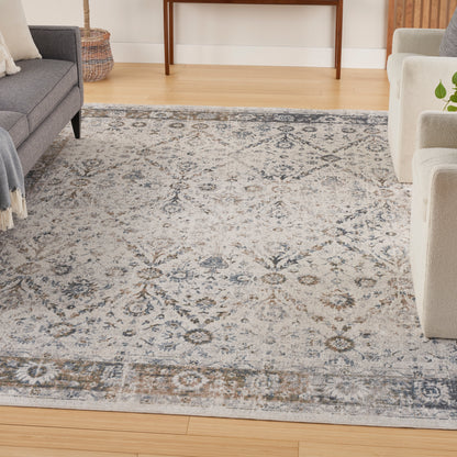 Grey and ivory patterned area rug in a contemporary living room with light wood floors, grey sofa and beige chairs.