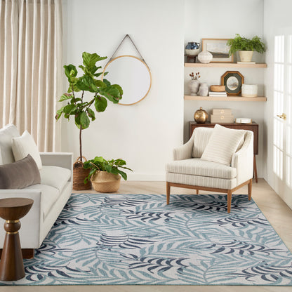 Neutral living room with blue leafy rug, cream sofa and armchair, potted plants, and round wall mirror.
