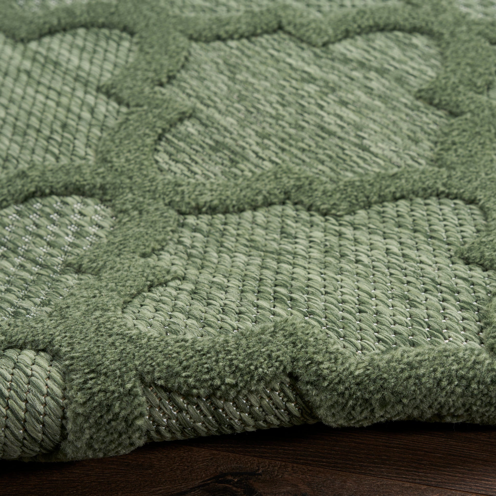 Close-up of a sage green rug with chunky looped texture and raised geometric motif.