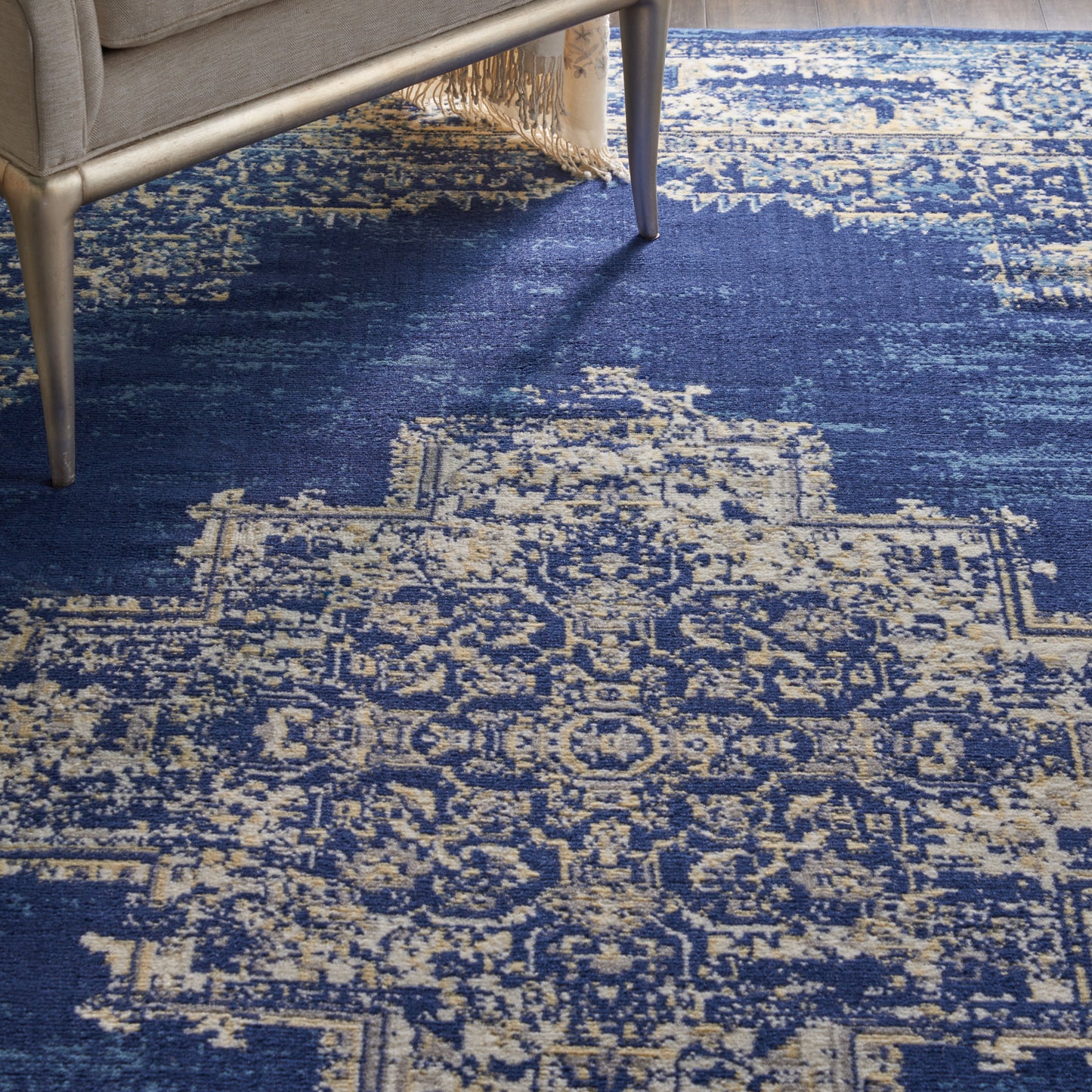 Navy blue oriental area rug with ivory distressed pattern under a light sofa with fringed edge.
