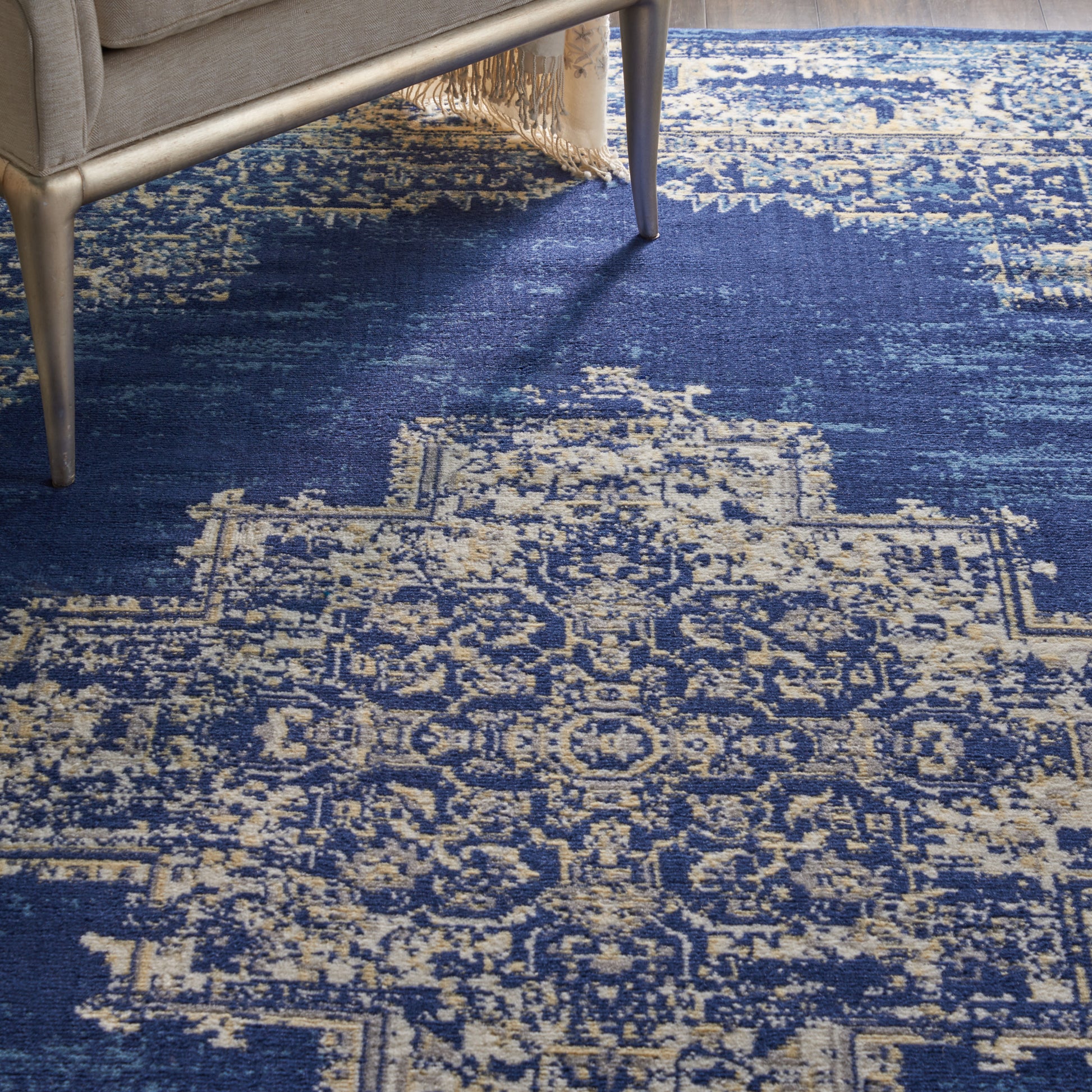 Navy blue oriental area rug with ivory distressed pattern under a light sofa with fringed edge.