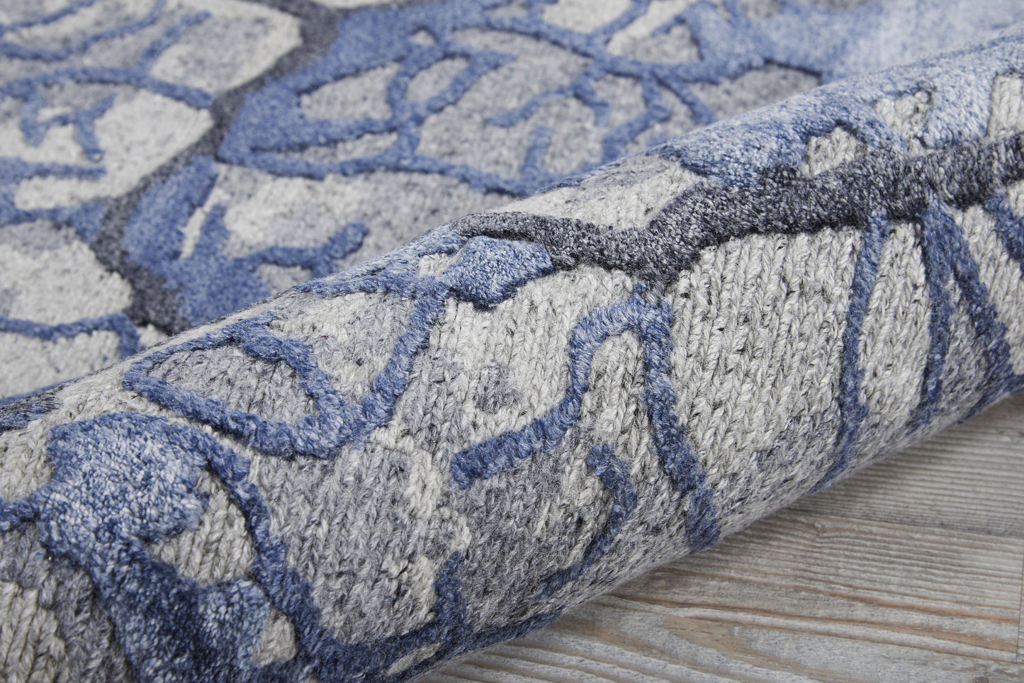Blue & gray patterned rug with abstract motif, plush pile, rolled on a wooden floor.