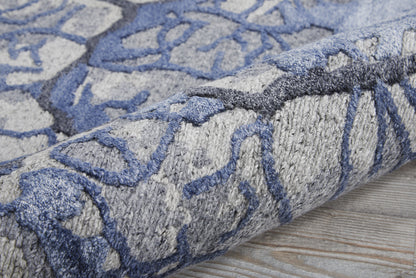 Blue & gray patterned rug with abstract motif, plush pile, rolled on a wooden floor.
