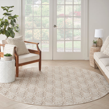 Round beige rug with subtle leaf pattern in a bright neutral living room; wooden armchair, woven side table, potted plants.