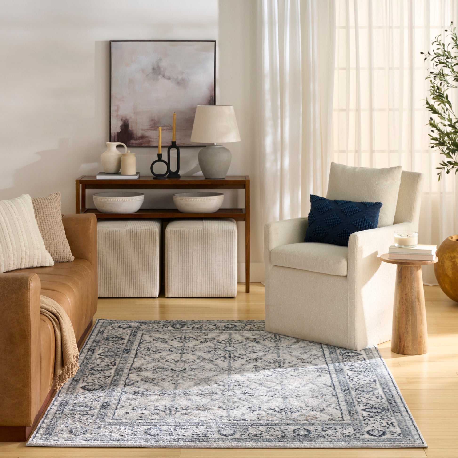 Cozy living room with tan leather sofa, blue throw pillow, abstract art, white ottomans, and patterned rug.