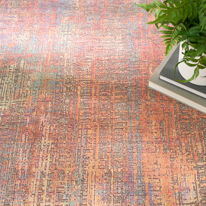 Orange-brown geometric patterned area rug with teal accents, beside a plant on a stack of books.