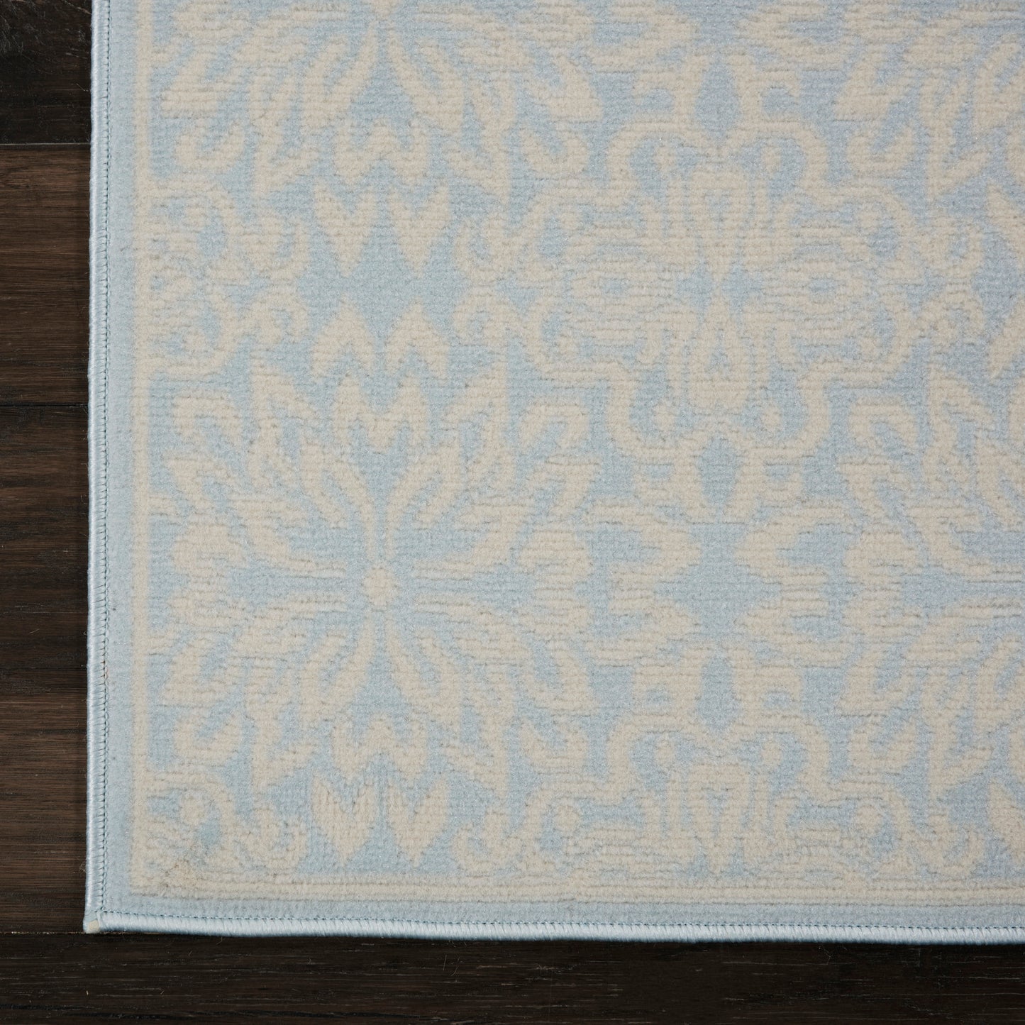 Powder-blue rug with cream damask pattern and pale border on dark wooden floor.