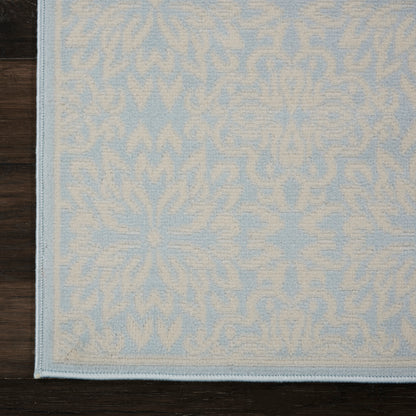 Powder-blue rug with cream damask pattern and pale border on dark wooden floor.