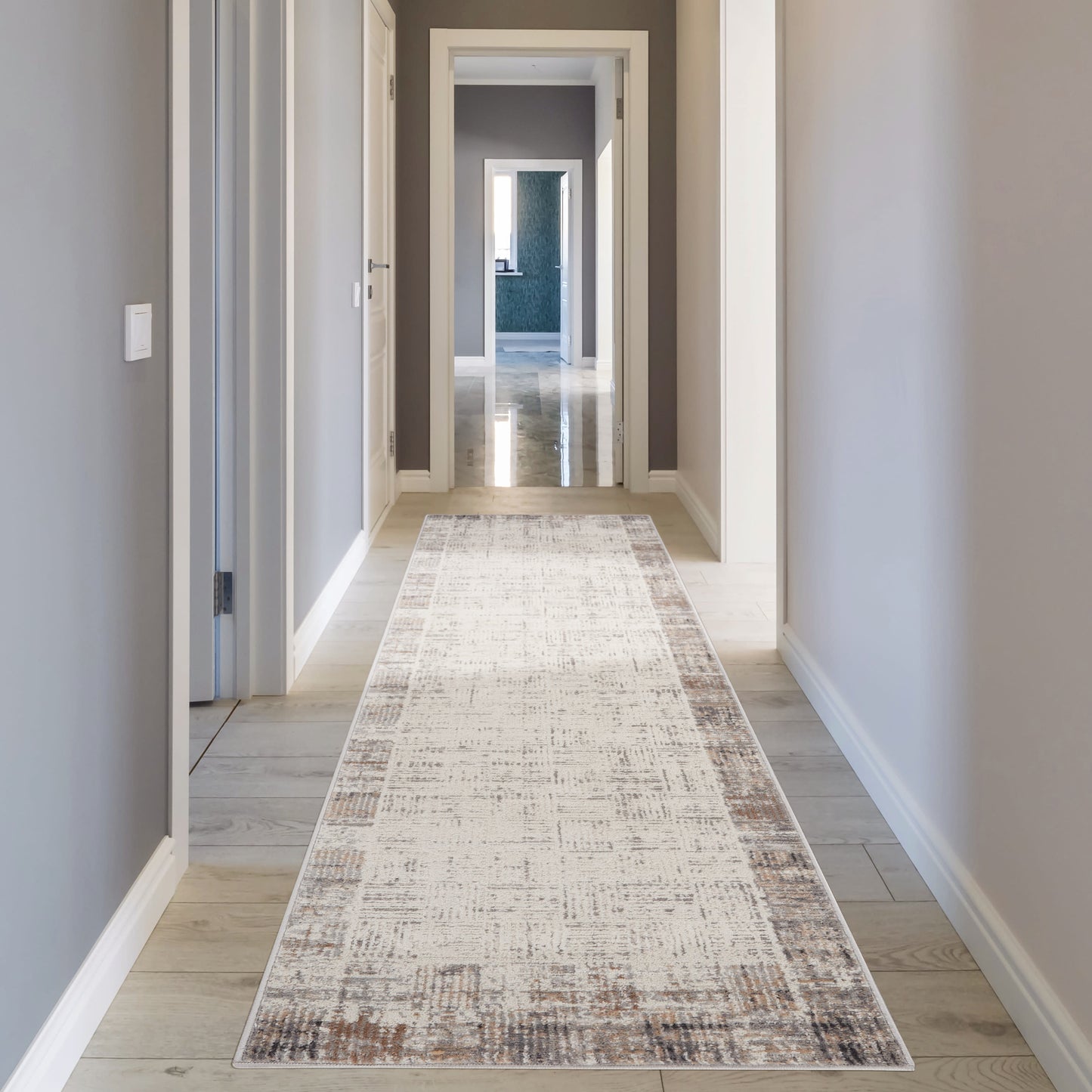 Long gray-walled hallway with white trim, light wood flooring, and a beige distressed runner rug.