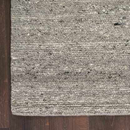 Close-up of a gray speckled loop-pile rug on dark wood floor.
