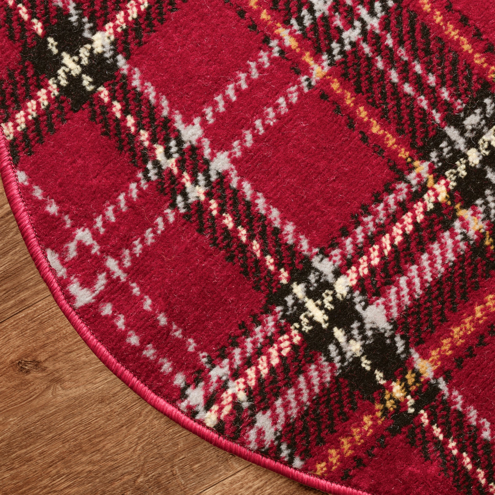 Red plaid Christmas round rug with black, white and yellow stripes, pink edging, fuzzy wool texture on wood floor.