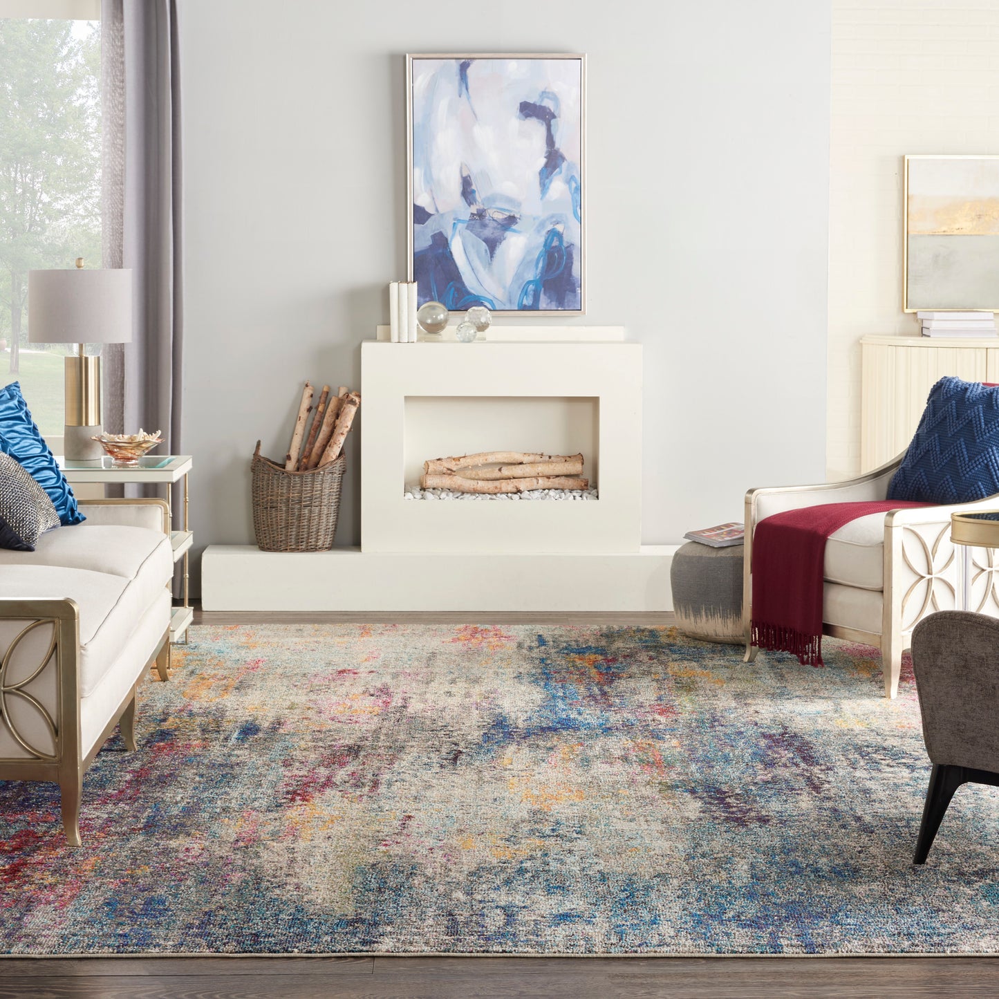 Modern white fireplace with logs, abstract blue artwork, multicolor rug, cream sofas and blue pillows in a cozy living room.