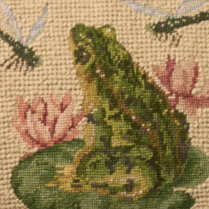 Tapestry textile with a green frog on a lily pad among pink flowers, beige woven background; rustic home decor.