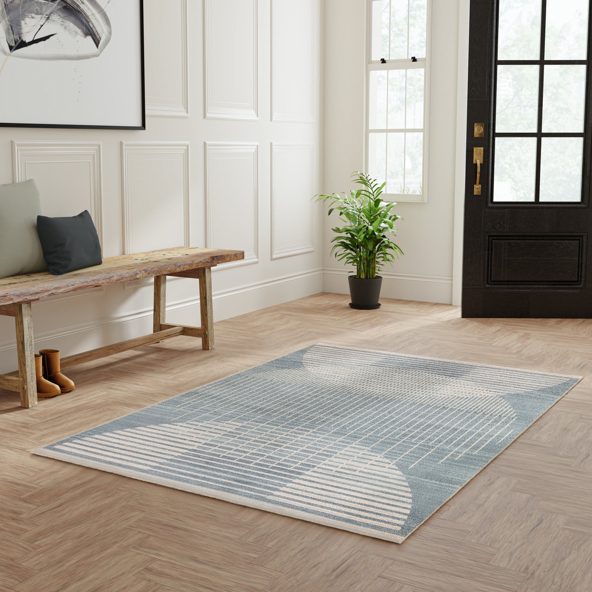 Blue-gray geometric area rug with curved white lines on a light wood hallway floor; bench, plant, and black-framed door.