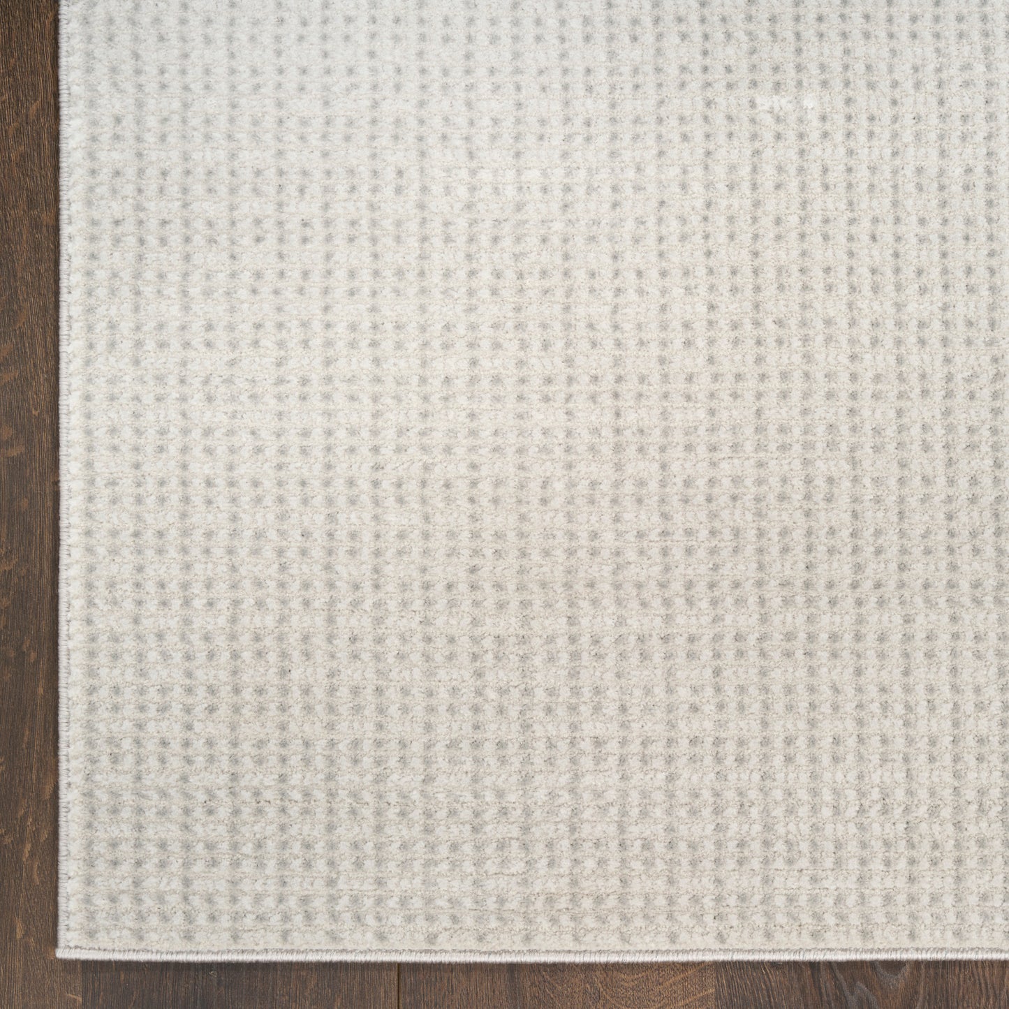 Cream textured woven rug with a subtle grid pattern on dark wood flooring.