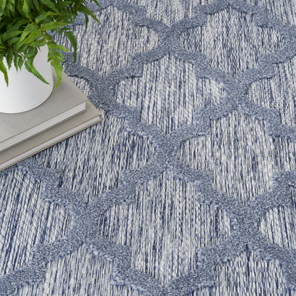 Blue-gray geometric trellis rug with textured weave; plant in white pot and stacked neutral books nearby.
