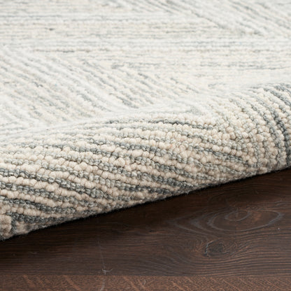 Soft, low-pile area rug in pale gray and ivory with subtle chevron pattern, rolled edge on dark wood floor.