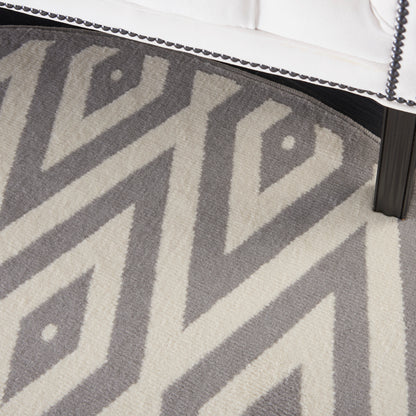 Gray & cream chevron geometric round rug under a white upholstered bed frame with nailhead trim & black leg.