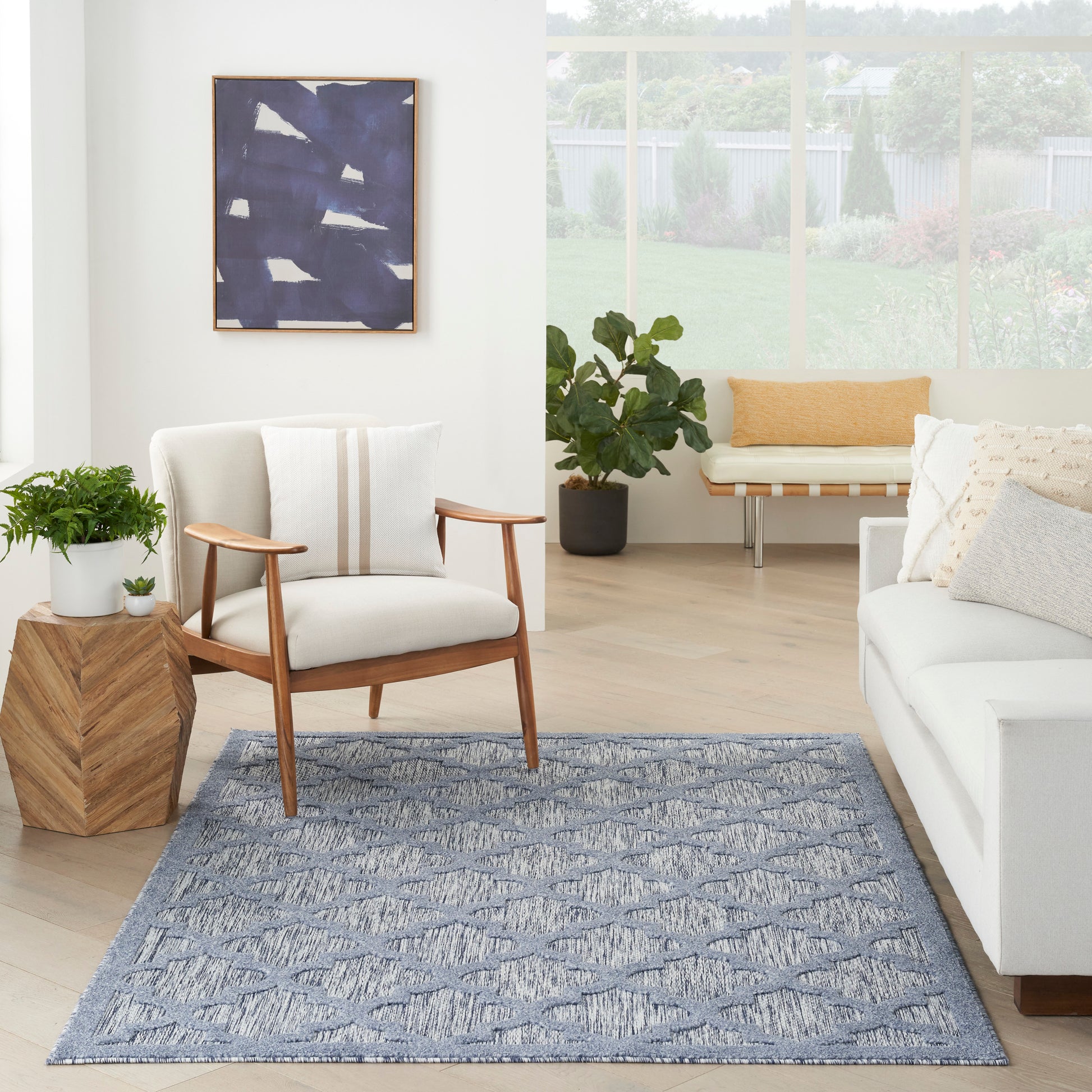 Blue patterned area rug in a bright living room with white sofa and mid-century chair, plants, and abstract wall art.