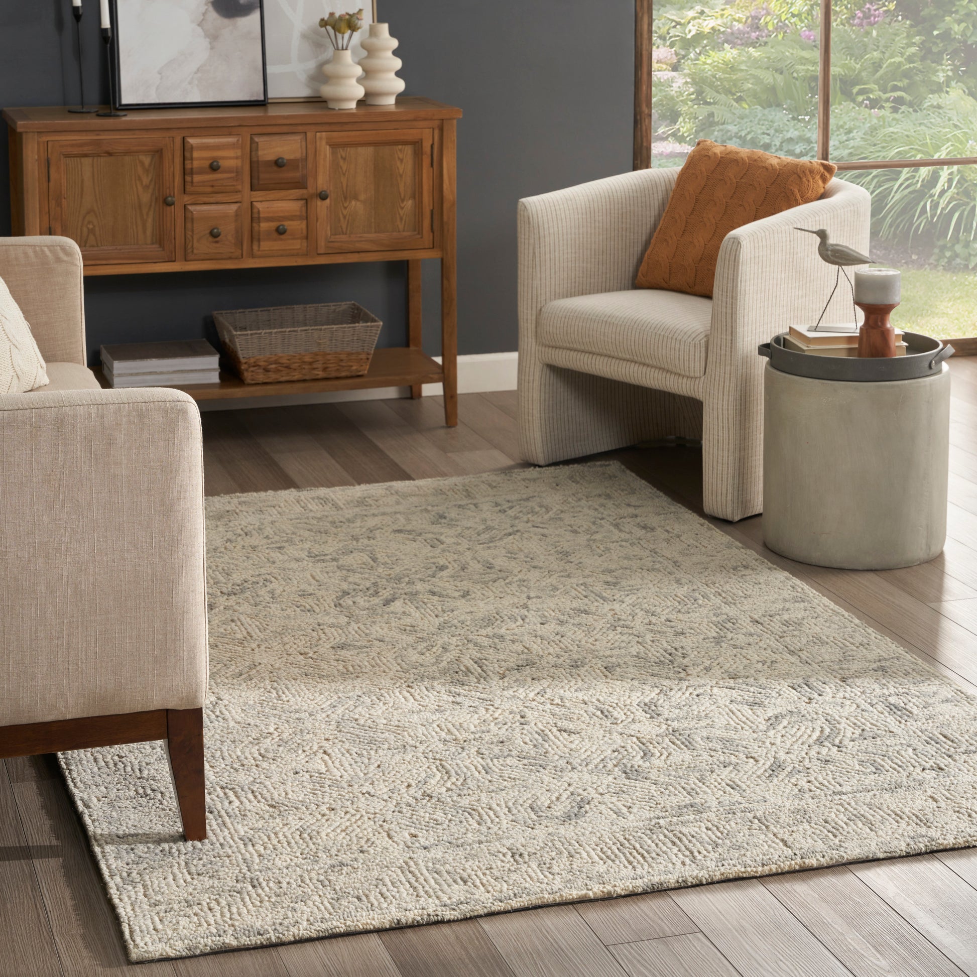 Beige textured rug in a room setting; wooden console, wicker basket, and round concrete side table with a bird statue.