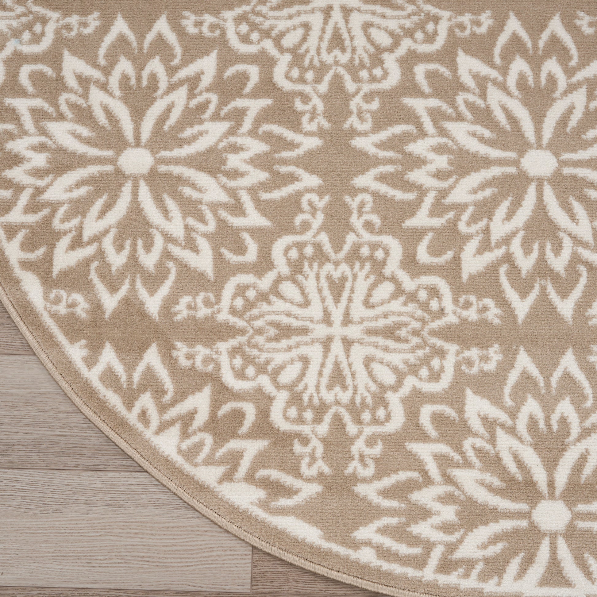 Round beige rug with white mandala-style medallion pattern on light wood floor.