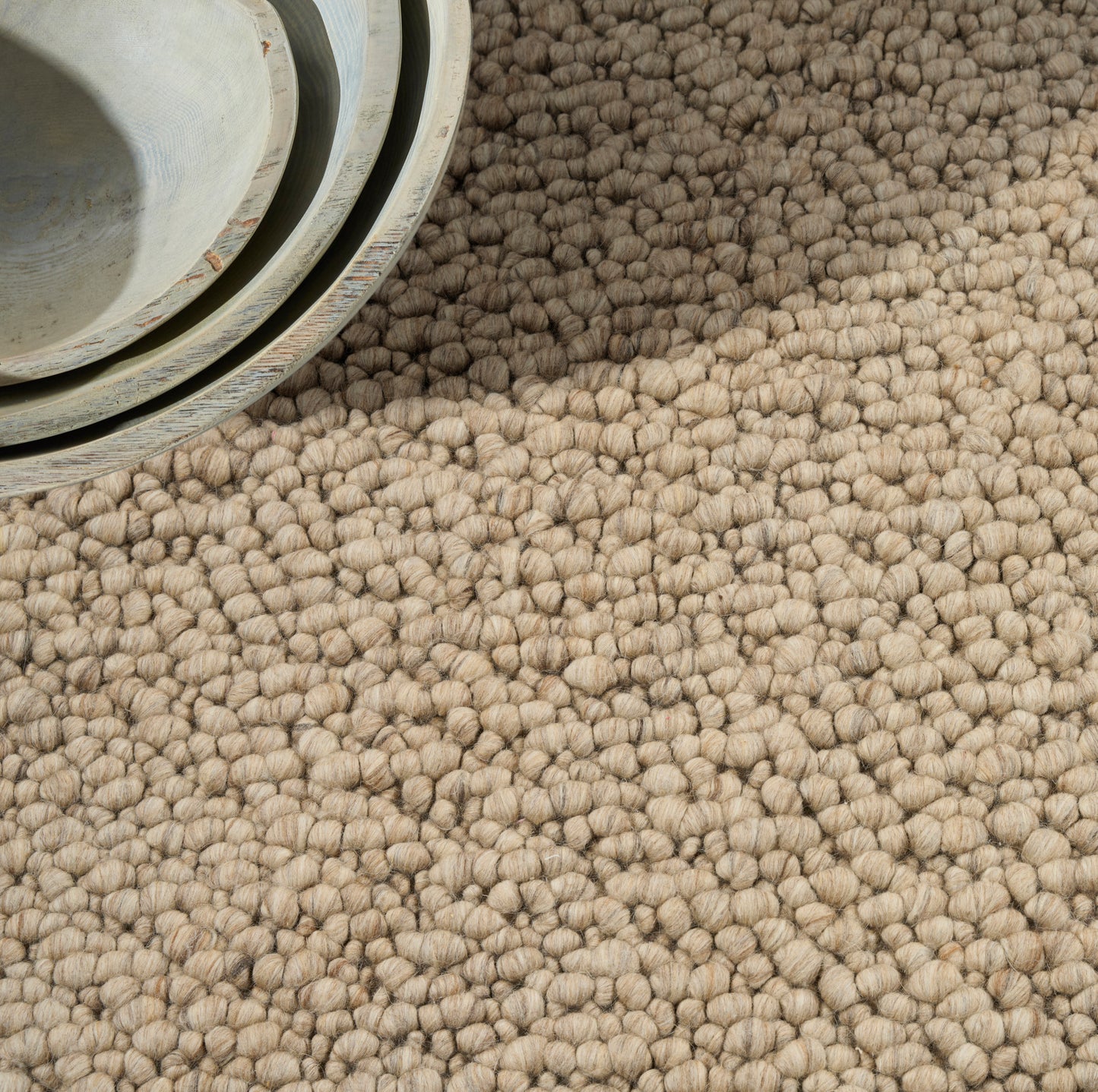 Beige chunky loop-pile rug texture with a light blue-grey rolled edge at the top-left.