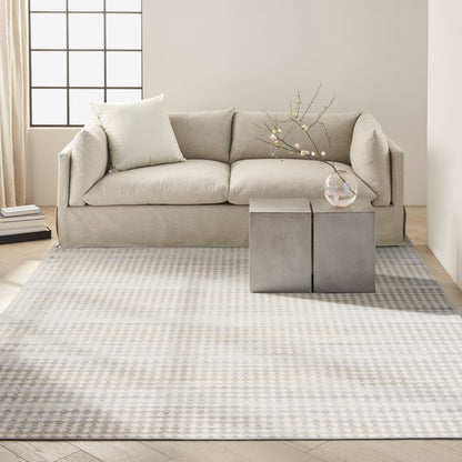 Beige fabric sofa in a bright living room with a pale checkered rug, concrete cube tables, and a glass vase of branches.