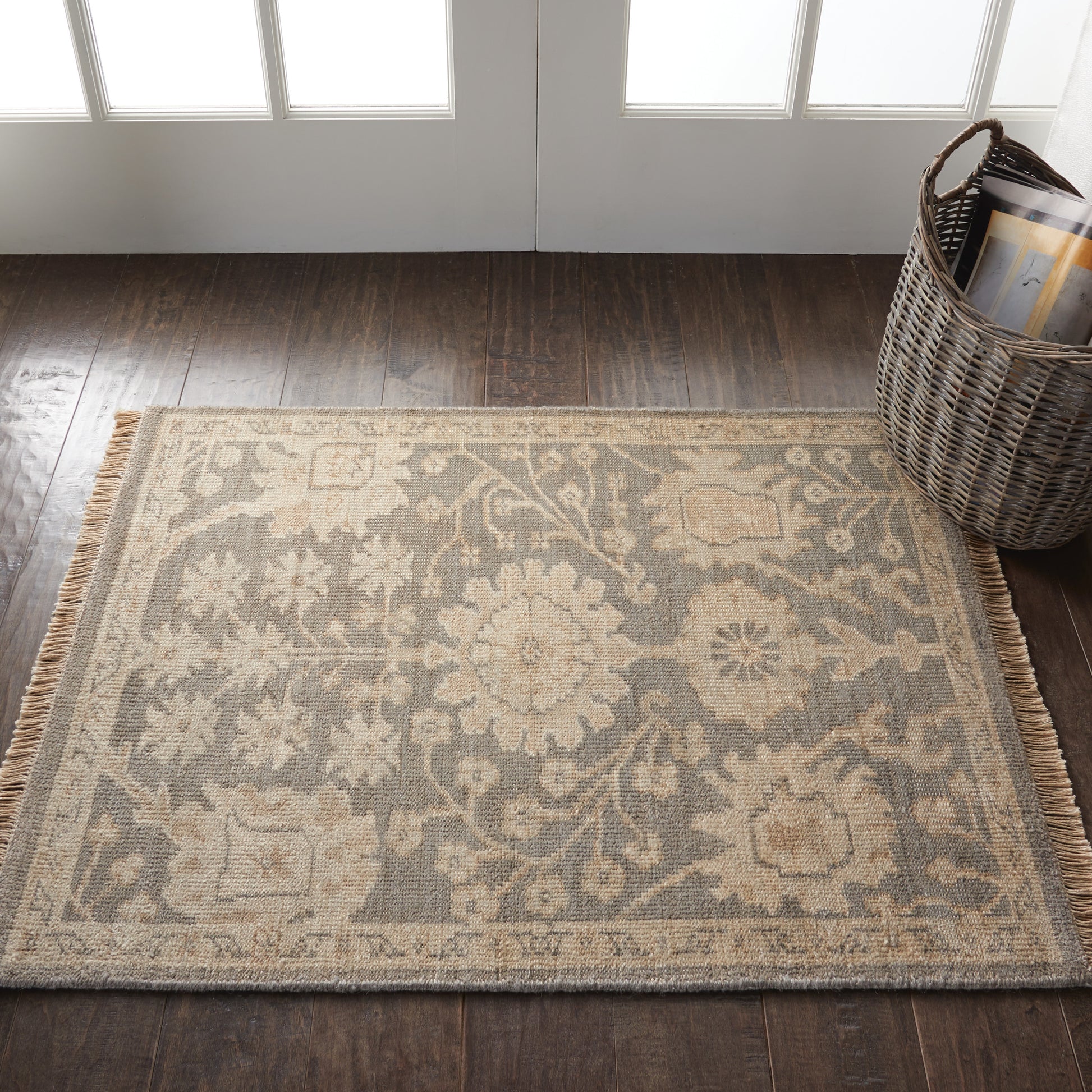 Beige and gray oriental-style area rug with floral medallions and fringe on dark wood floor beside a wicker basket.
