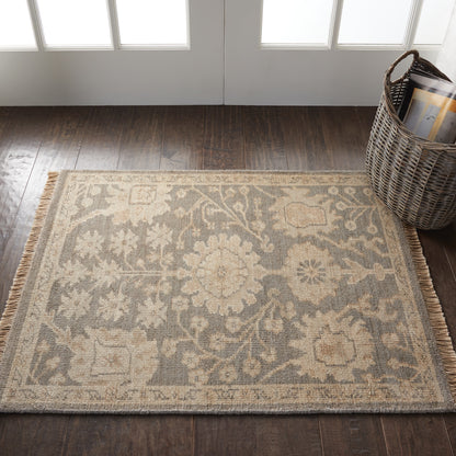 Beige and gray oriental-style area rug with floral medallions and fringe on dark wood floor beside a wicker basket.