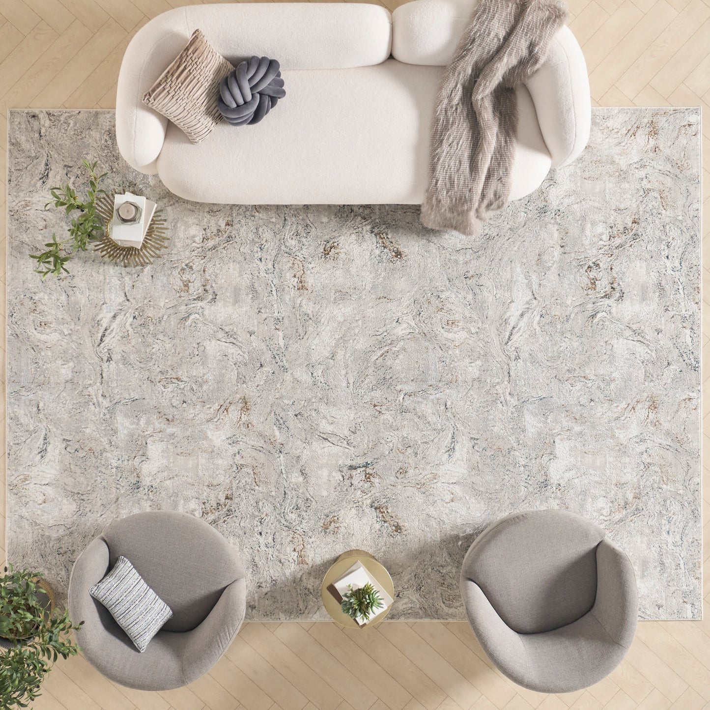 Large light-gray marble-pattern rug in a neutral living room with cream sofa, gray armchairs, throw, and plants.