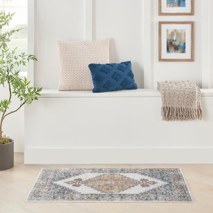 Blue-gray diamond rug 2' x 4' with a beige fringed throw, beige knitted cushion, and a blue textured cushion nearby.