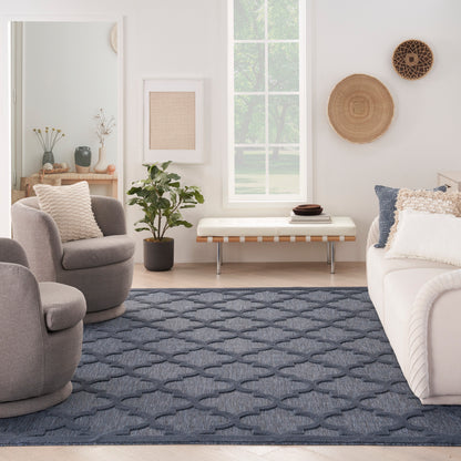 Bright living room with gray rounded lounge chairs, white sofa, navy rug, plant, wall art, wicker wall decor.
