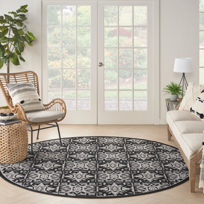 Round black-and-white contemporary patterned rug in a bright living room with wicker chair, beige sofa, plants and French doors.