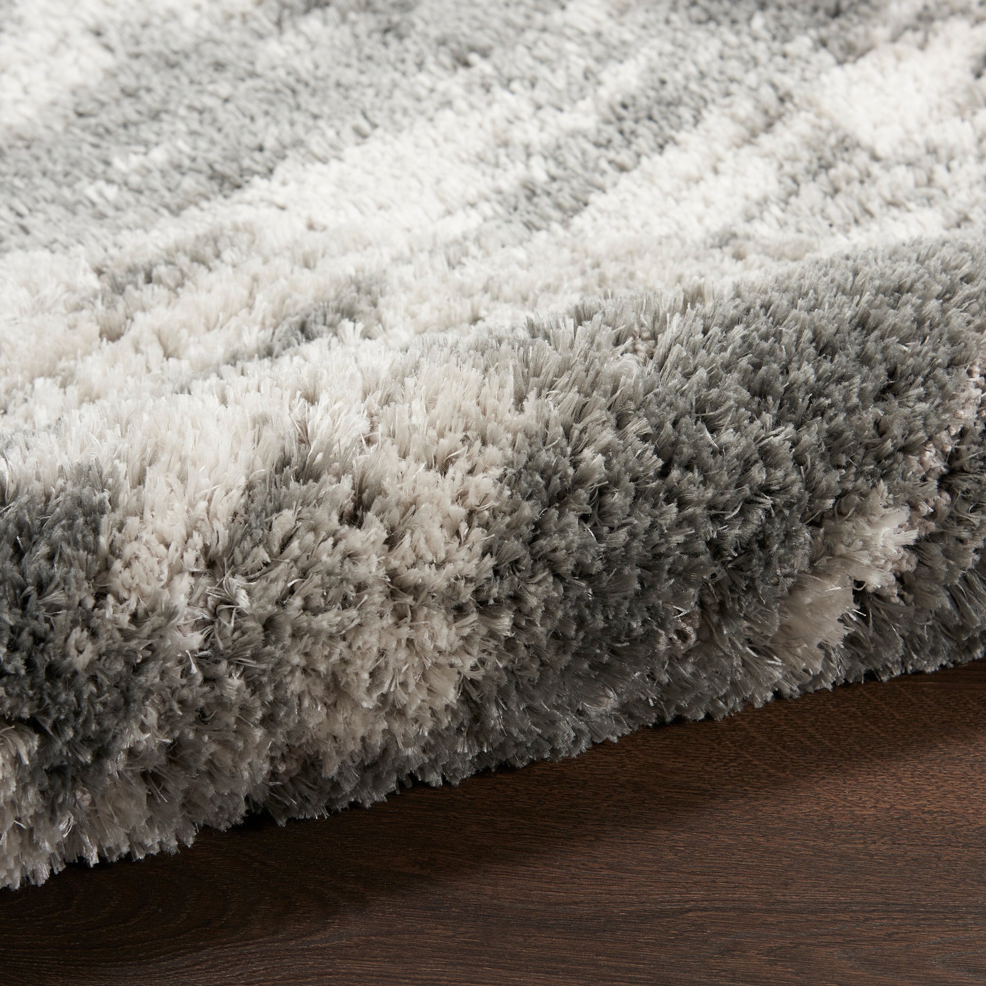 Fluffy gradient shag rug in ivory to charcoal tones, laid on dark wood floor.