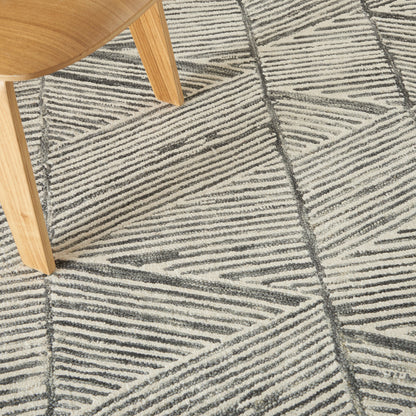 Light wooden chair leg with curved seat on a textured beige and gray geometric rug with diagonal stripe pattern.
