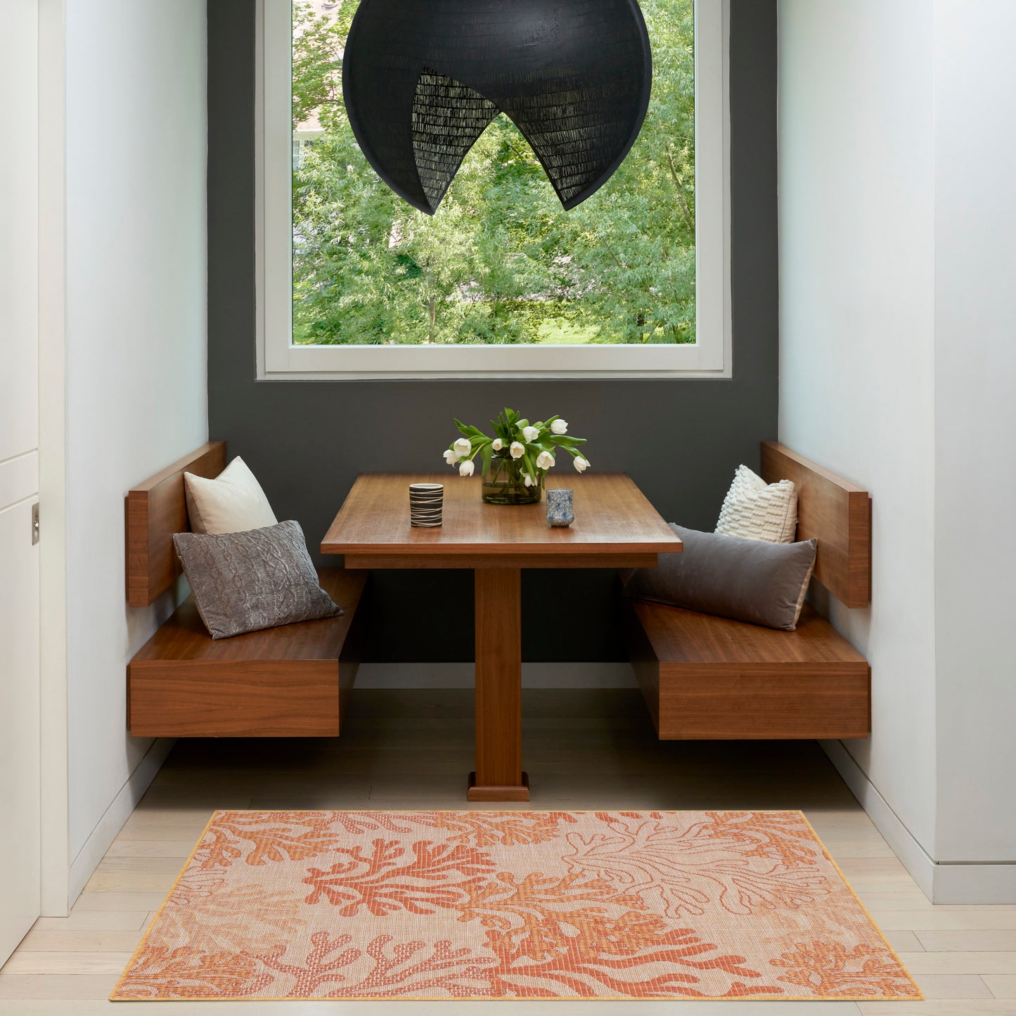Cozy wooden dining nook with benches, square table, gray walls, peach rug, black pendant lamp, floral centerpiece.